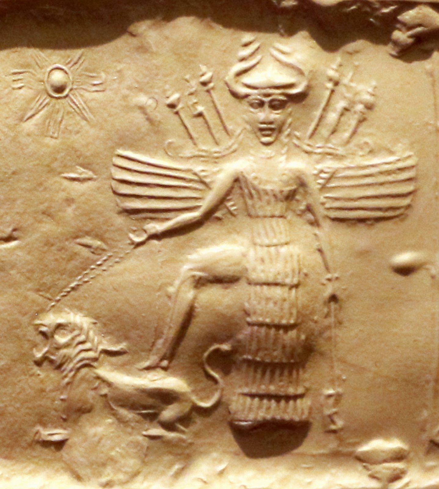 Impression of an Akkadian cylinder seal, 2350-2150 BC, showing the winged goddess Ishtar armed with weapons on her back, wearing a horned helmet, and standing with one foot on a lion.