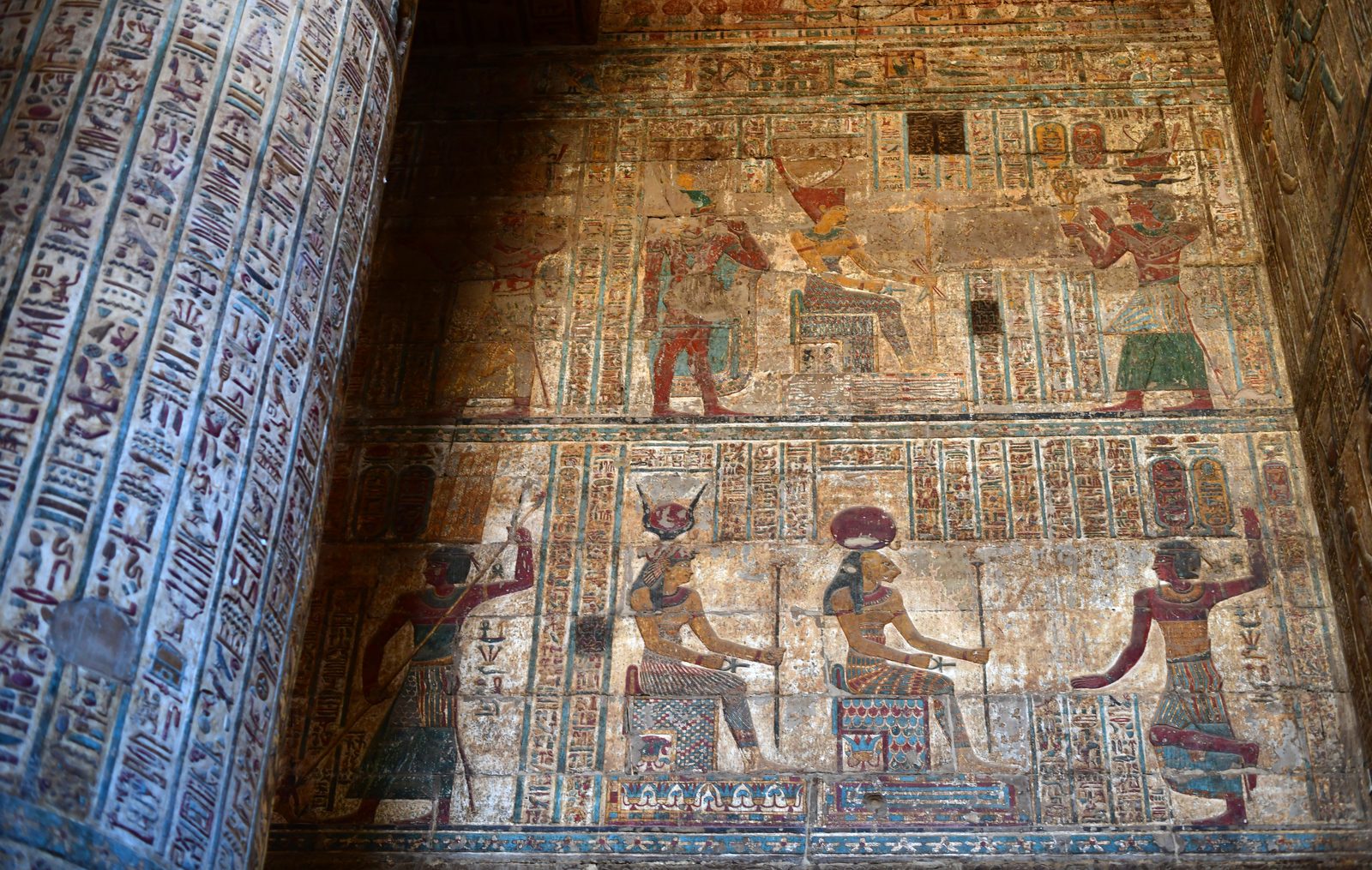 Colorful painted reliefs inside the Temple of Khnum at Esna, showing ram-horned deities among rows of hieroglyphic inscriptions.