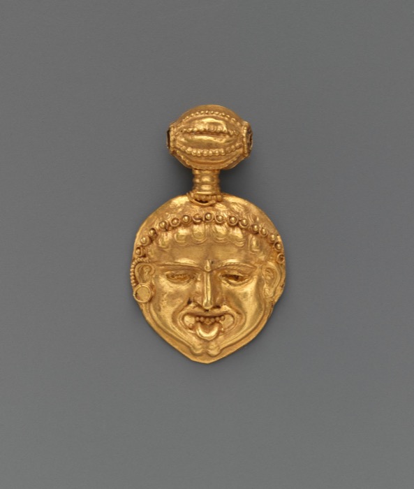 A small gold pendant in the form of a gorgoneion, showing the stylized wide-eyed face of a Gorgon, made in ancient Greece around 450 BCE and worn as personal protective jewelry.