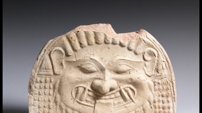 A terracotta gorgoneion antefix from an ancient Greek temple roof, showing the wide-eyed, wide-mouthed face of a Gorgon used as a protective architectural ornament, dated about 580-570 BCE.